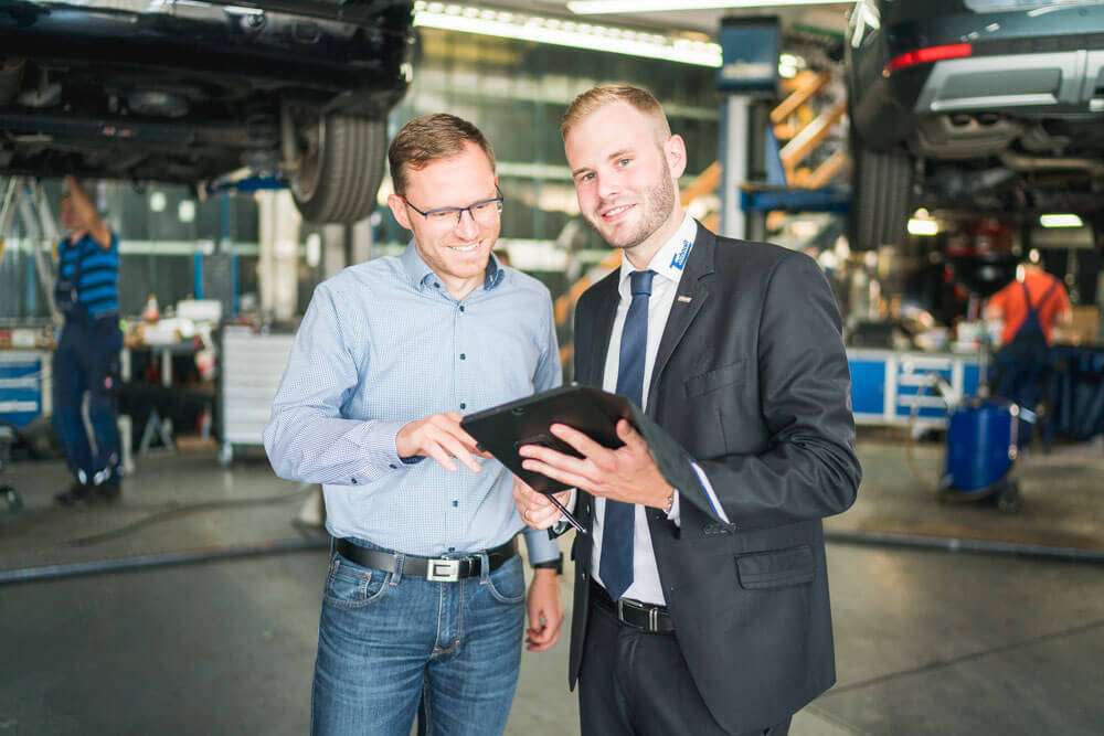 Zwei Männer stehen in einer Autowerkstatt und schauen gemeinsam auf ein Tablet.