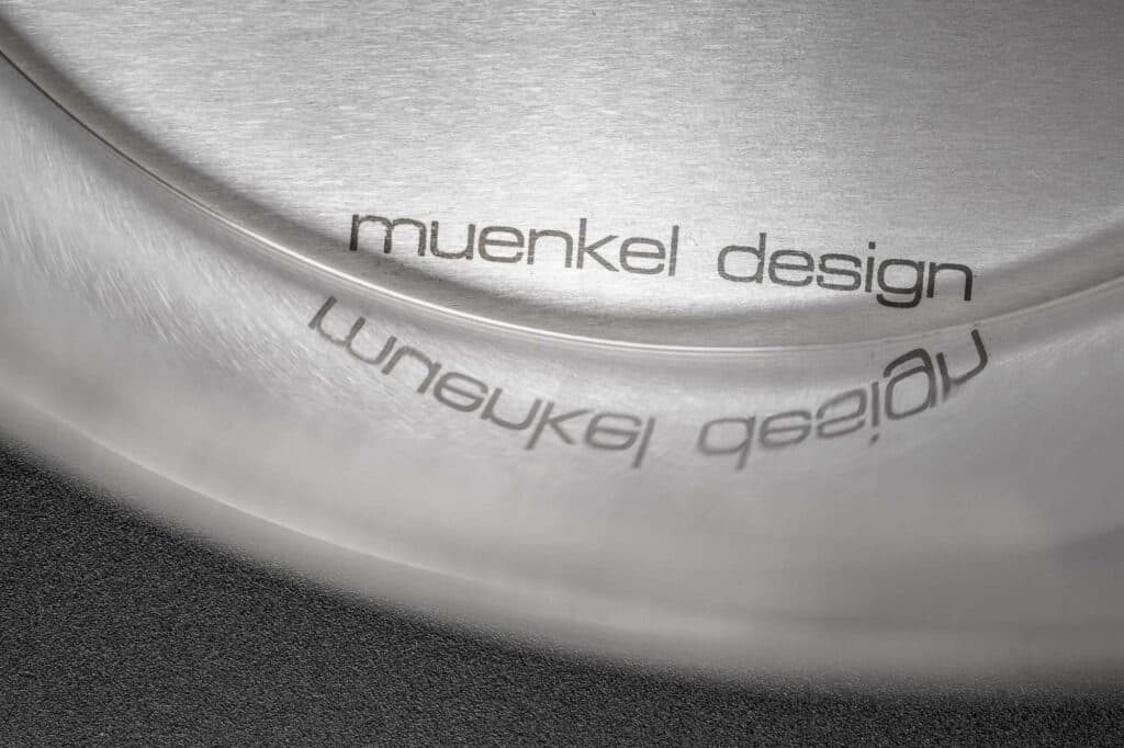 Nahaufnahme eines eingravierten Firmenlogos auf einer glänzenden Metalloberfläche mit einer deutlichen Spiegelung des Schriftzugs.