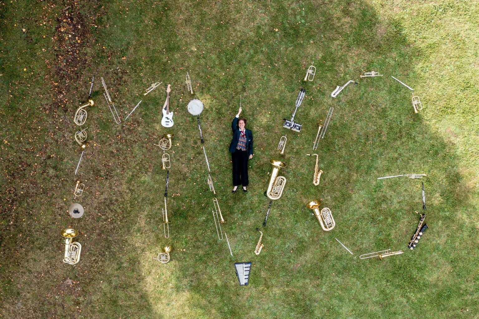 Eine Person liegt auf einer grünen Wiese und ist von verschiedenen Musikinstrumenten umgeben, die in ihrer Anordnung den Schriftzug LOVE bilden, aufgenommen aus der Vogelperspektive.
