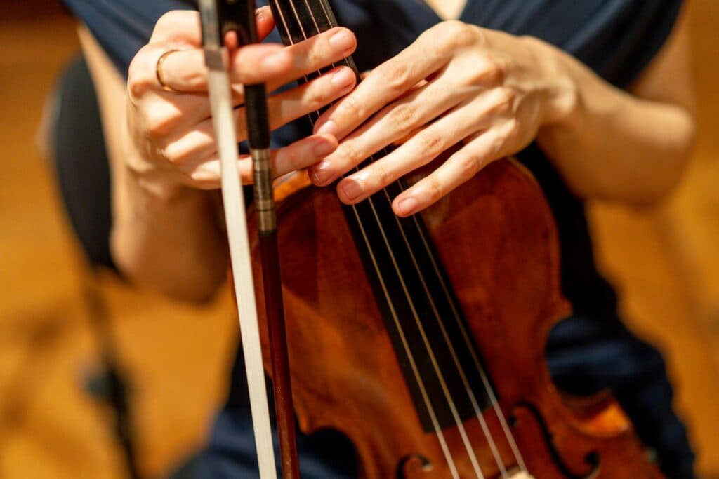 Nahaufnahme der Hände einer Musikerin, die eine Geige und einen Bogen hält.