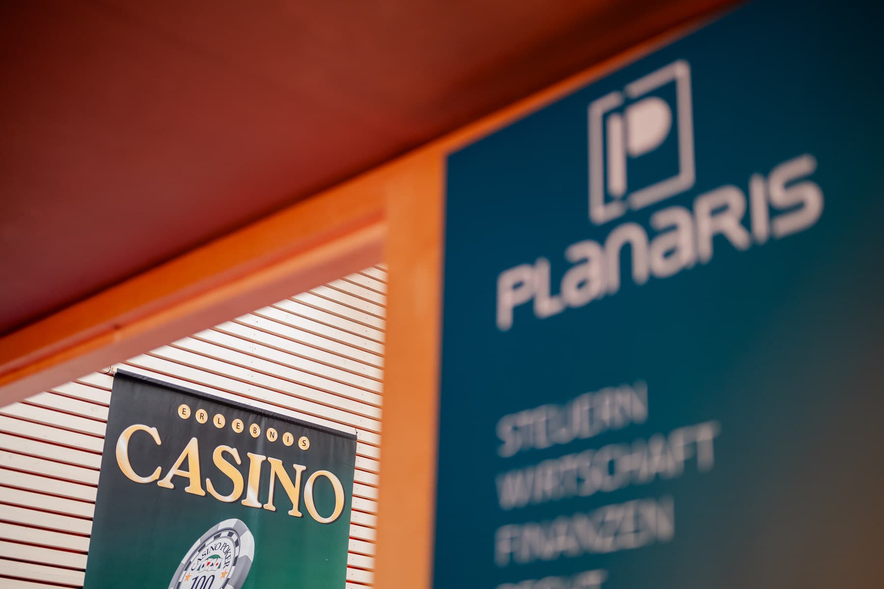 Zwei Werbeschilder mit den Aufschriften Planaris und Casino hängen an einer Fassade, wobei das vordere Schild unscharf und das hintere Schild scharf dargestellt ist.