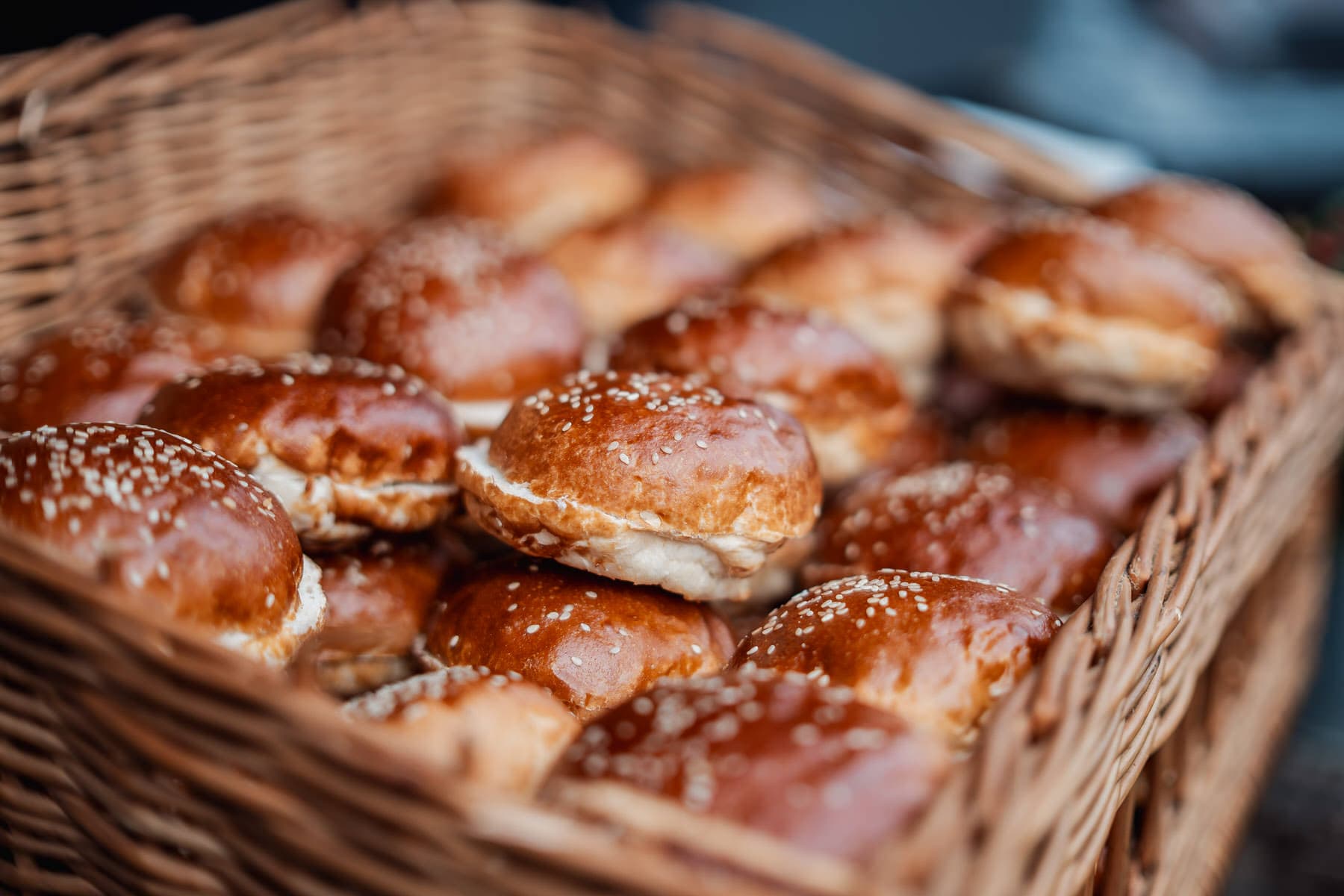 Ein geflochtener Weidenkorb gefüllt mit vielen glänzenden, mit Sesam bestreuten Brötchen.