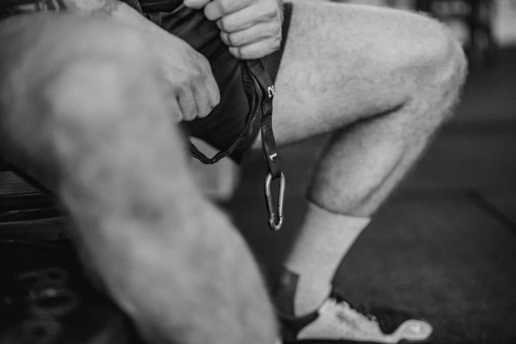 Nahaufnahme der Beine und Hände einer Person in Sportkleidung, die einen Karabinerhaken hält.