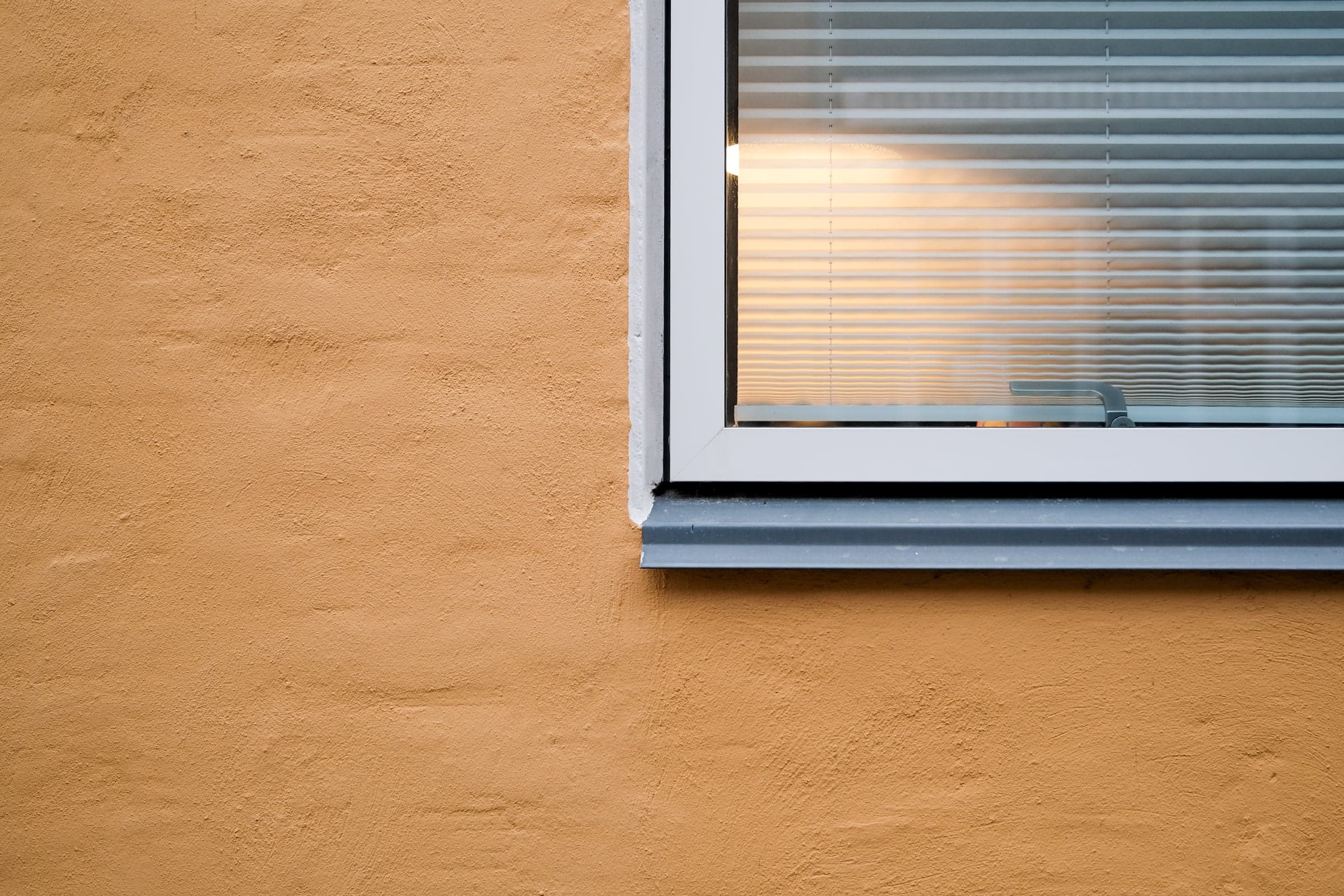 Warmes Licht hinter einer Jalousie in einer gelben Fassade