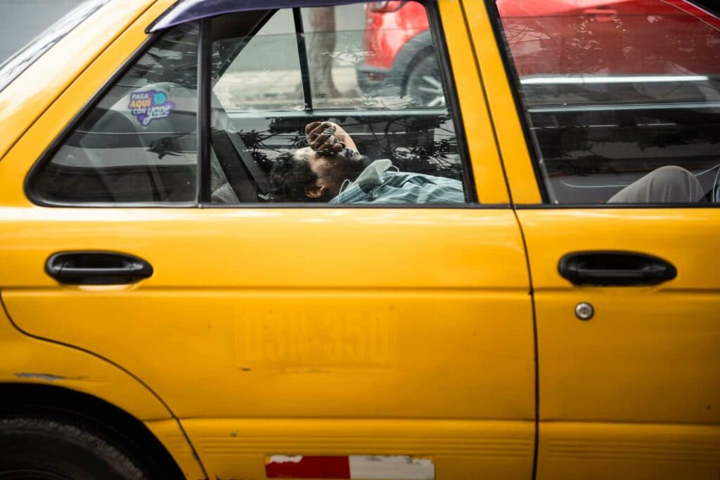 Ein gelbes Taxi von der Seite gesehen, durch dessen Fenster eine schlafende Person auf dem Rücksitz zu erkennen ist.