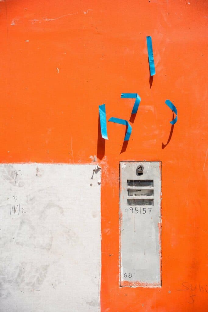 Eine leuchtend orangefarbene Wand mit einem grauen Briefkasten und aufgeklebten blauen Klebestreifen.