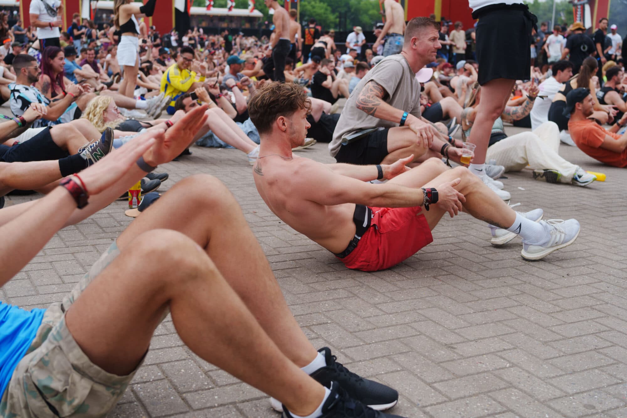 Eine große Gruppe von Menschen sitzt auf einem gepflasterten Platz und führt gemeinsam Fitnessübungen aus.