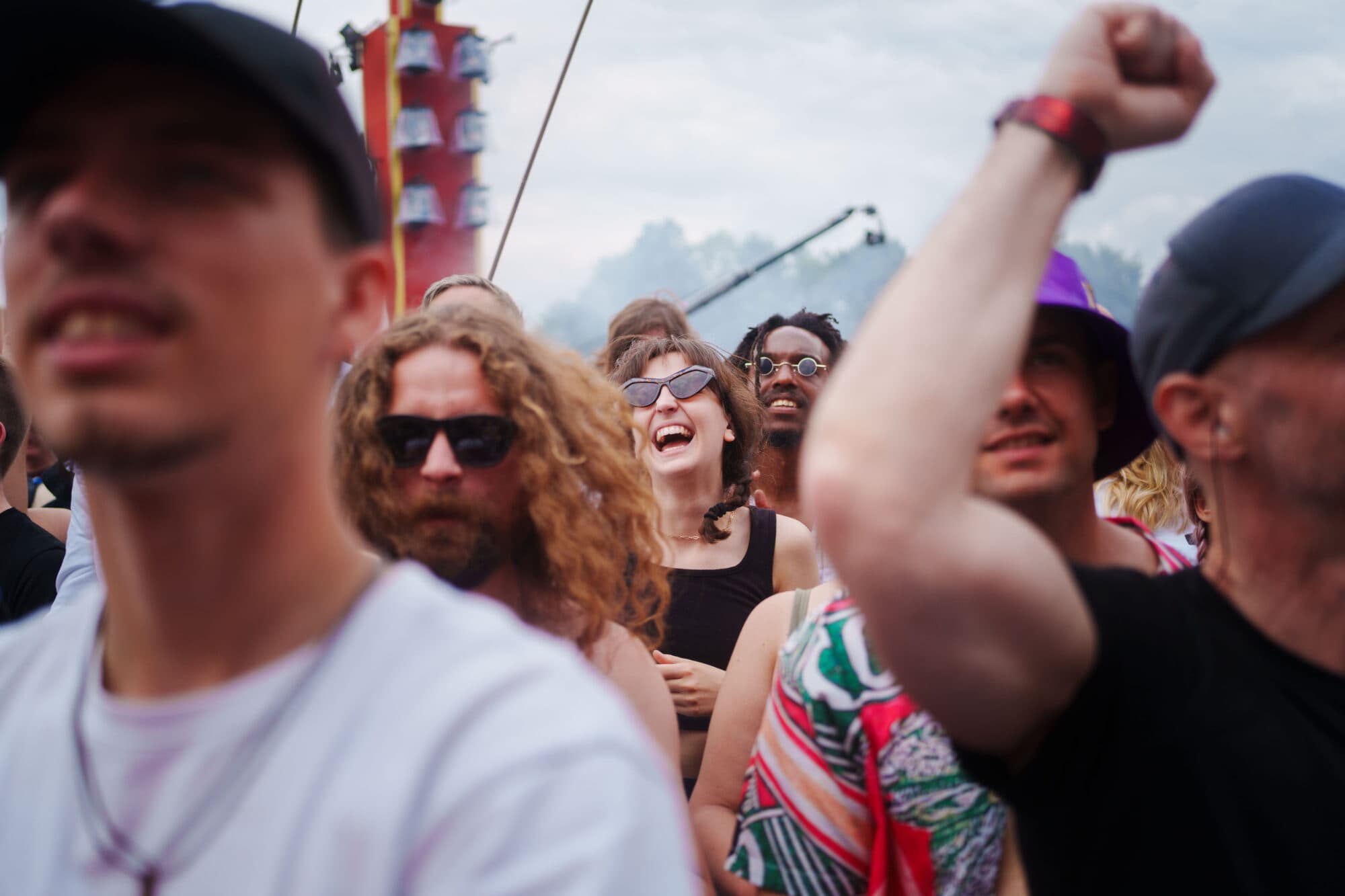 Eine Gruppe junger Menschen feiert auf einem Festival, wobei eine Person im Vordergrund den Arm in die Höhe streckt.