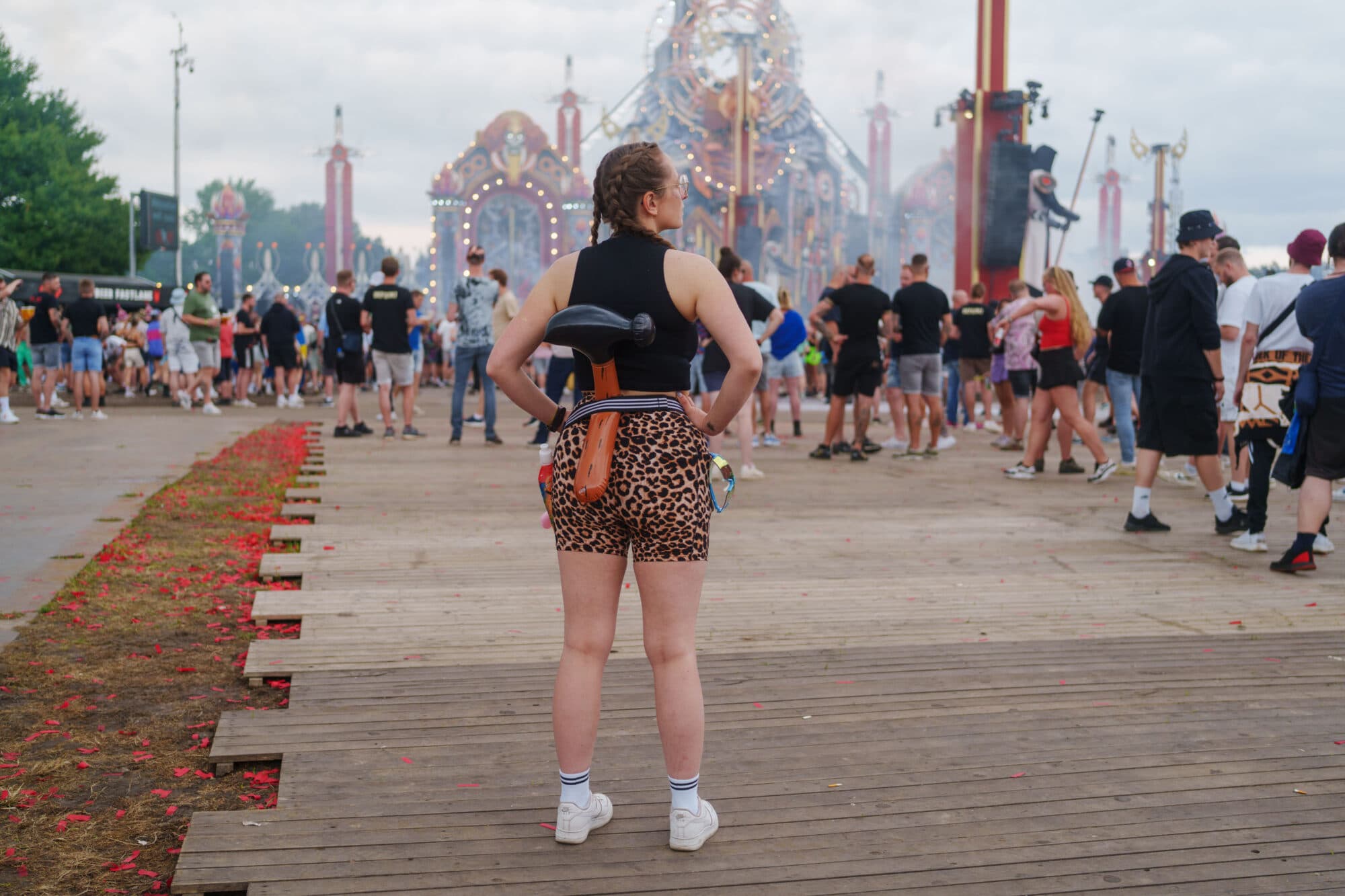 Eine Frau steht mit dem Rücken zur Kamera auf einem Holzboden vor einer großen Festivalbühne, umgeben von vielen anderen Menschen.