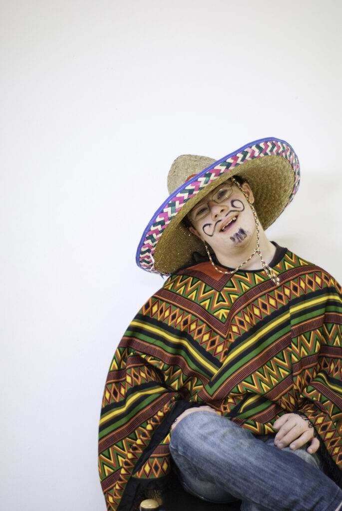 Eine Person trägt einen großen Sombrero und einen gemusterten Poncho, das Gesicht ist mit einem aufgemalten Schnurrbart verziert.