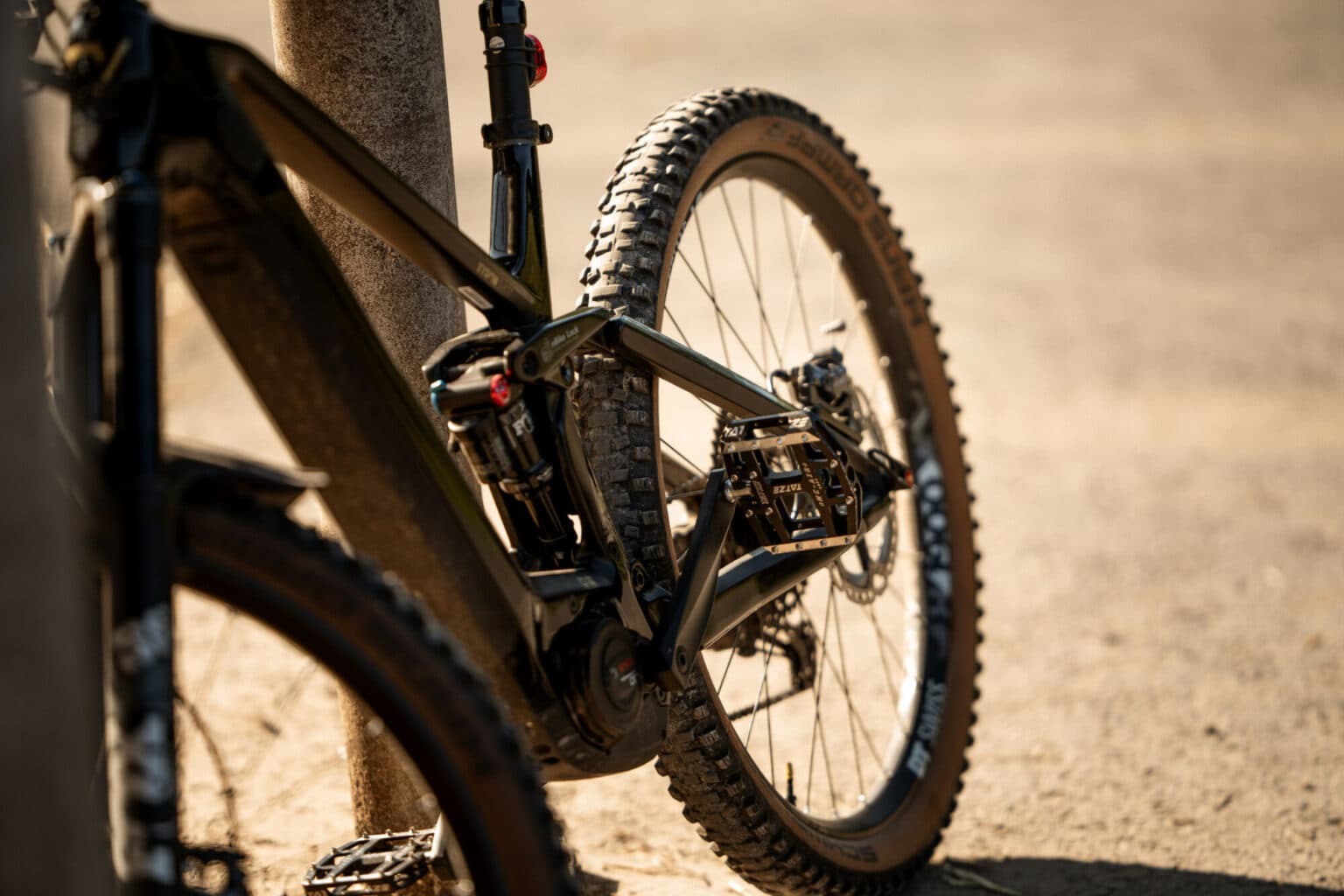 Ein schwarzes Mountainbike steht seitlich an einem Pfosten, wobei der Fokus auf dem Rahmen und dem Hinterrad liegt.